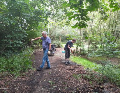 Two environmental volunteers clearing vegetation back from a curved path, located next to a seasonal pond.
